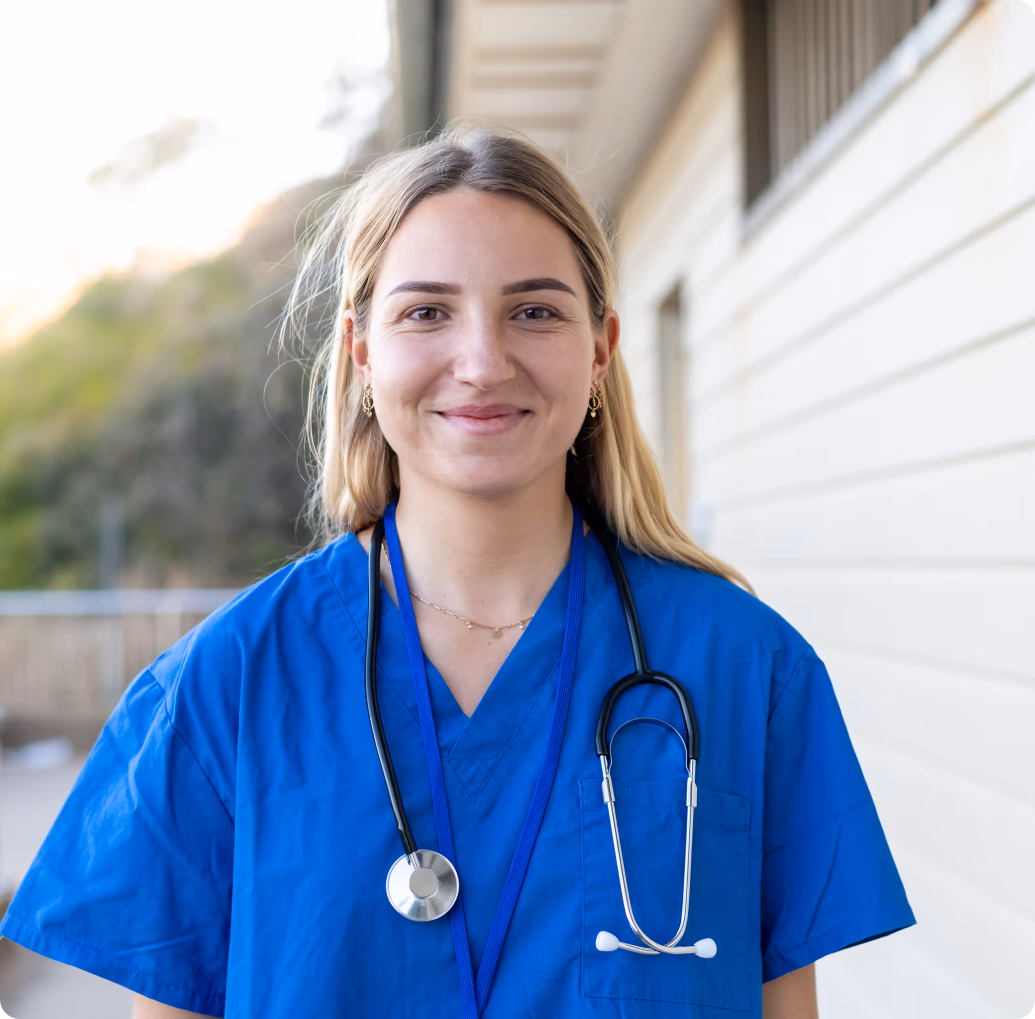 A young blonde haired lady with a blue medical shirt and a stethoscope