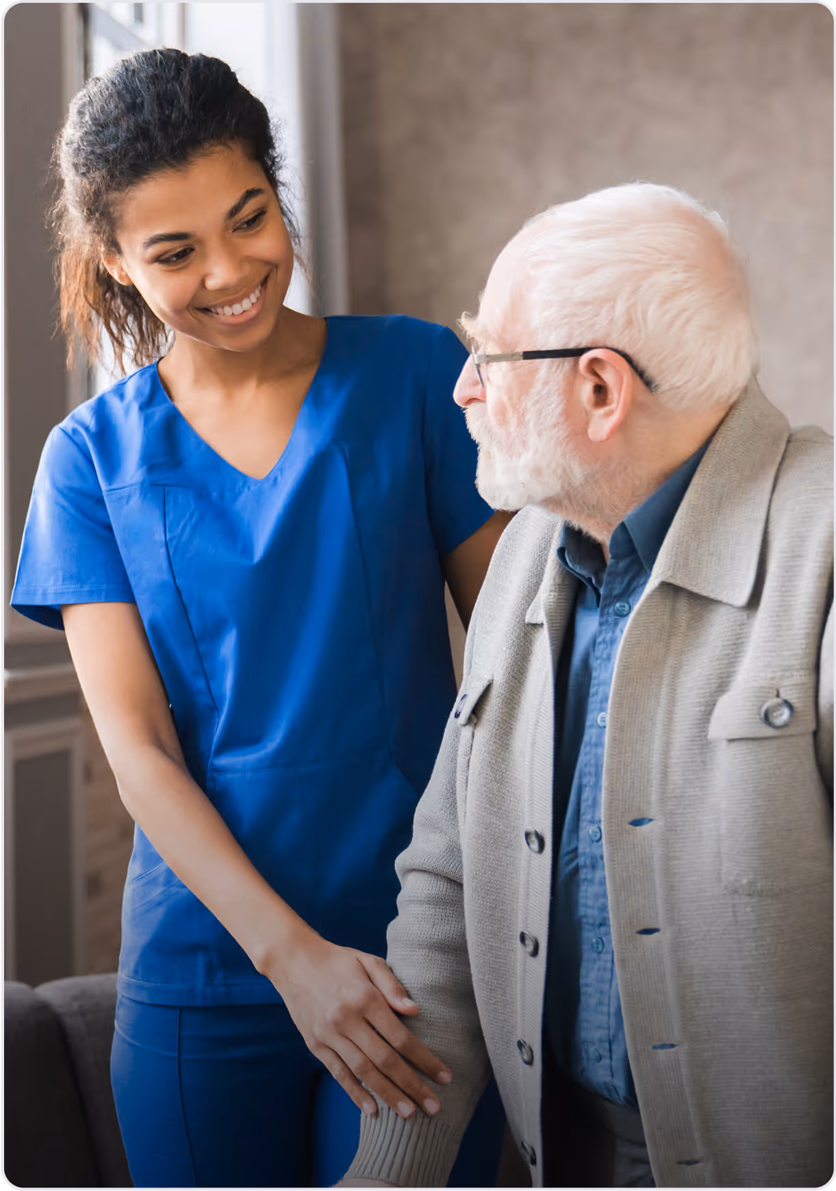 A lady carer in a blue shirt and pants standing next to an elderly gentleman.