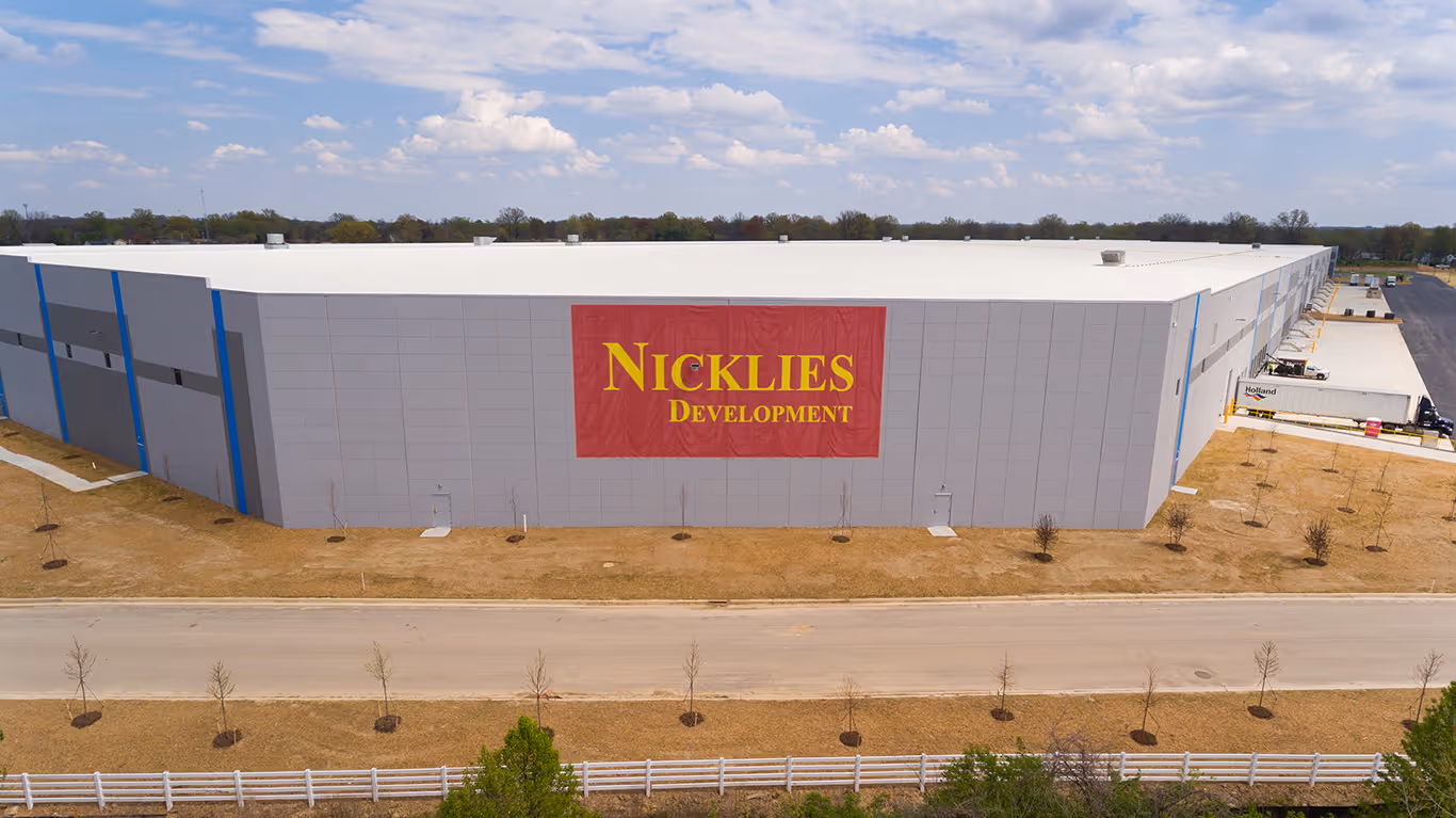 Large industrial building with a white roof and gray walls displaying a red banner with yellow text reading 'Nicklies Development'.