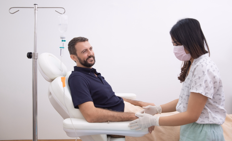 A man receives an IV infusion from a masked healthcare worker in a clinical setting. 