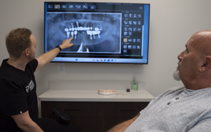 A dental professional discusses an X-ray with an older patient during a consultation, with an overlay showing a man holding a dental model.