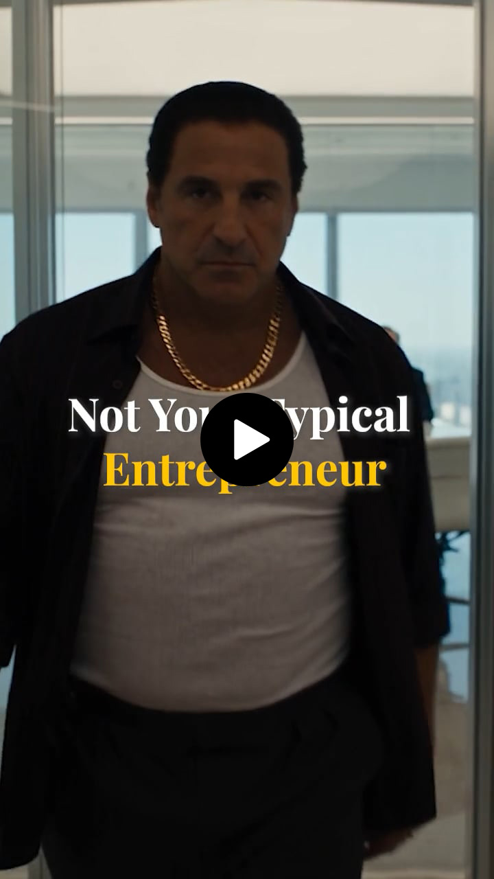 Man with dark hair wearing gold chain, white tank top, dark shirt walking indoors with text overlay.