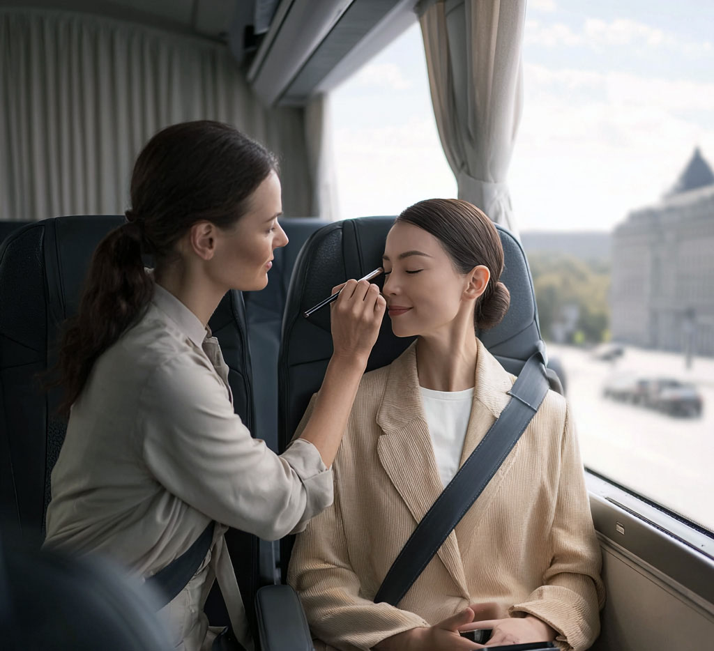 Woman applying makeup to another woman sitting by a bus window with city view.