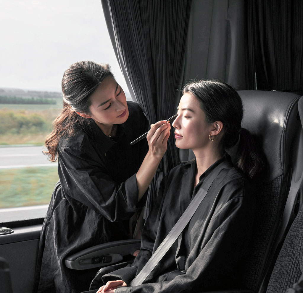 A female beauty professional is providing makeup and hairstyling services to a customer on the bus.
