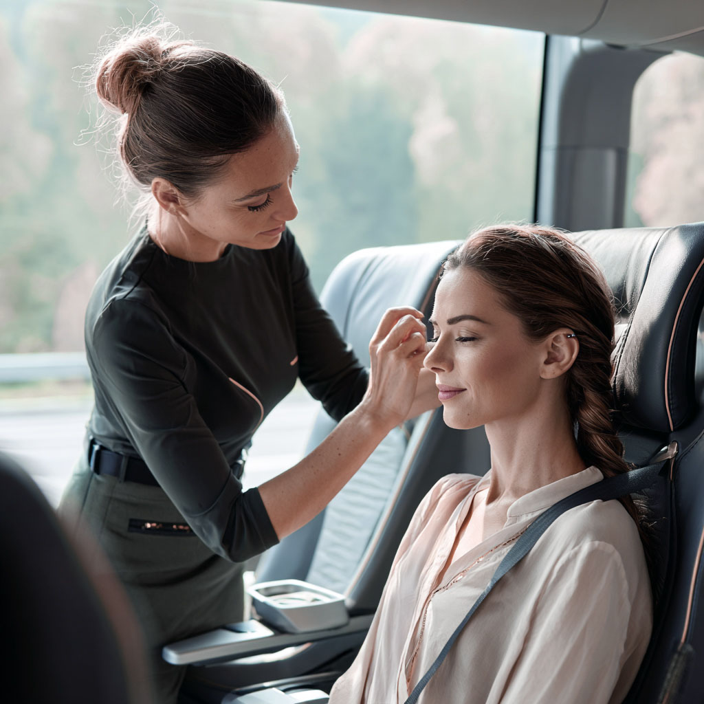 A female beauty professional is providing makeup and hairstyling service to a customer on the bus. 