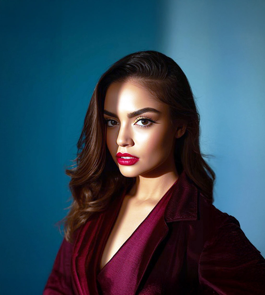 Woman with long brown hair wearing a dark red velvet jacket, lit by a strong shadow across her face against a blue background.
