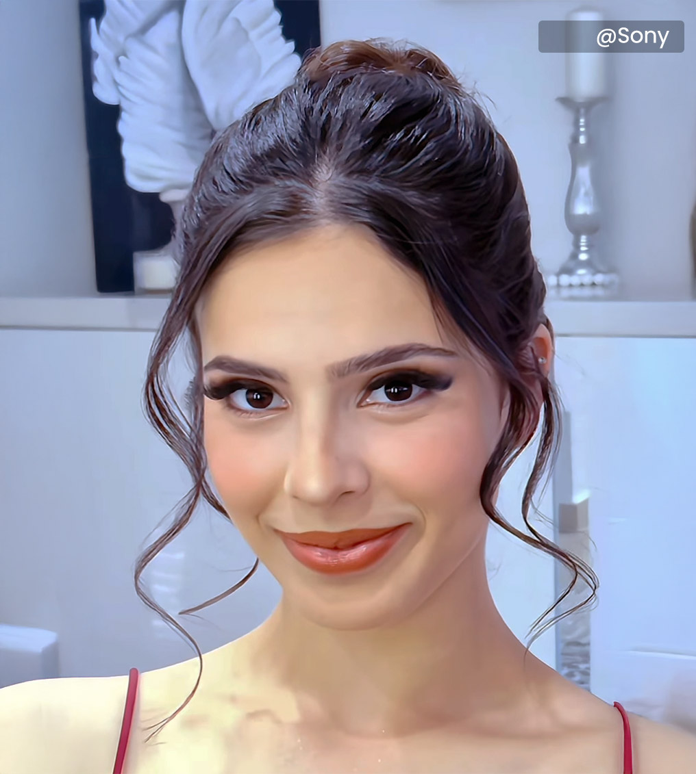 Young woman with vibrant rainbow eye makeup and glossy lips holding a cup filled with paintbrushes, wearing a yellow top.