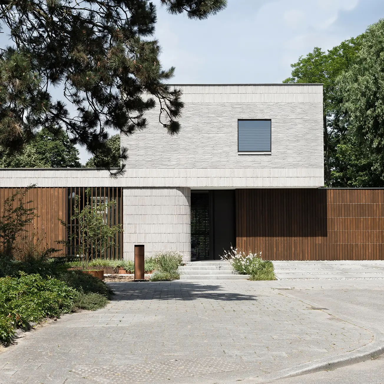 Modern two-story house with white brick upper level and wooden lower level surrounded by greenery.
