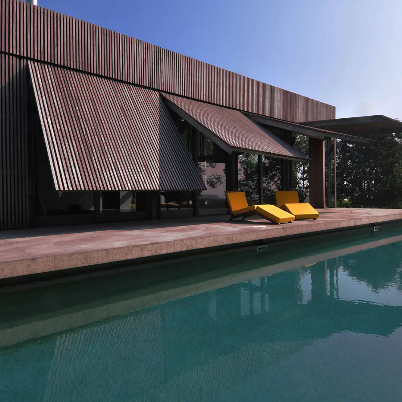 Modern house with wooden slatted exterior shutters open above a poolside patio with two bright yellow lounge chairs.