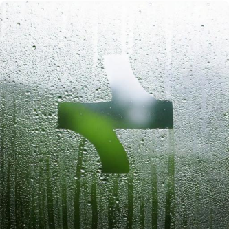 Window with condensation and water droplets, part of the glass wiped clear revealing a green and white background.