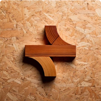 Four wooden blocks arranged on a textured plywood surface, forming an abstract geometric shape.