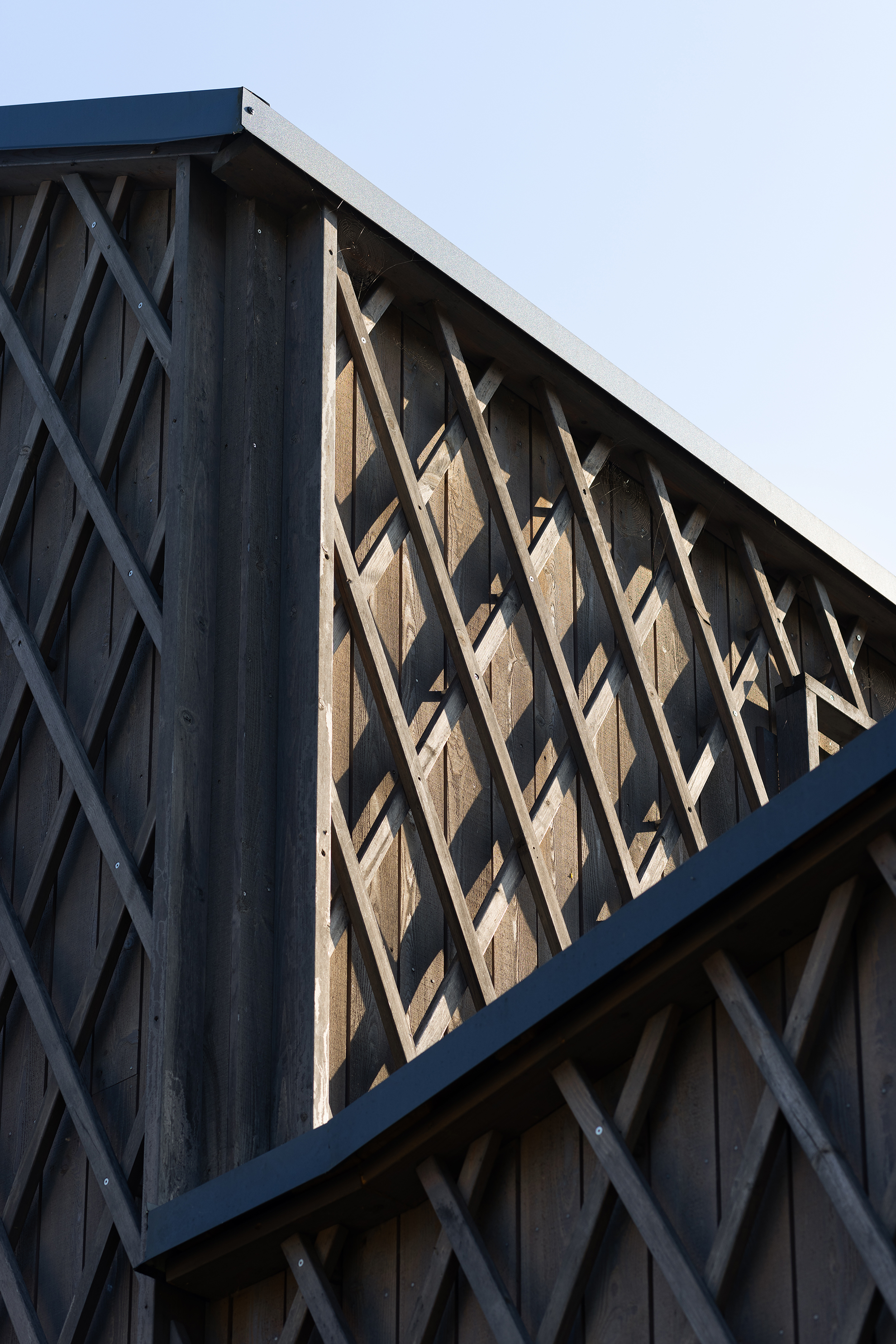 Close-up of a wooden building corner with diagonal latticework casting shadows in sunlight.