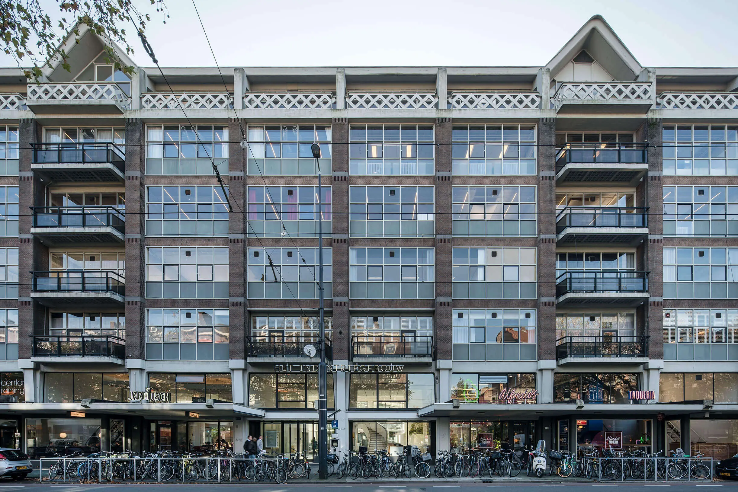 Modern multi-story building with large grid windows, balconies, bicycles parked in front, and ground-floor shops including Jarmusch and Alfredo's.