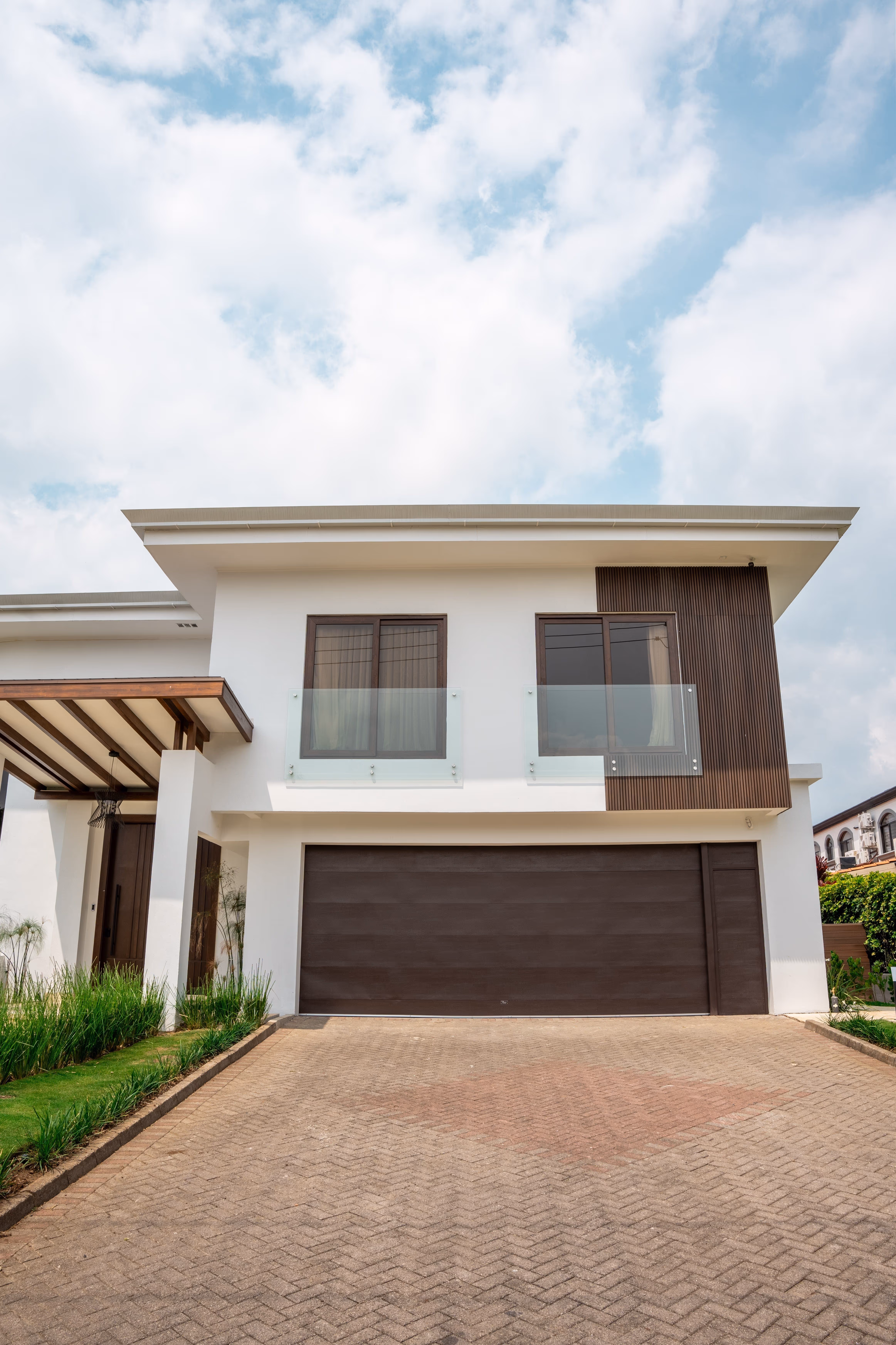 Fachada de casa moderna de dos pisos con garaje, puertas de vidrio de pvc imitación madera y balcón con barandales de vidrio.