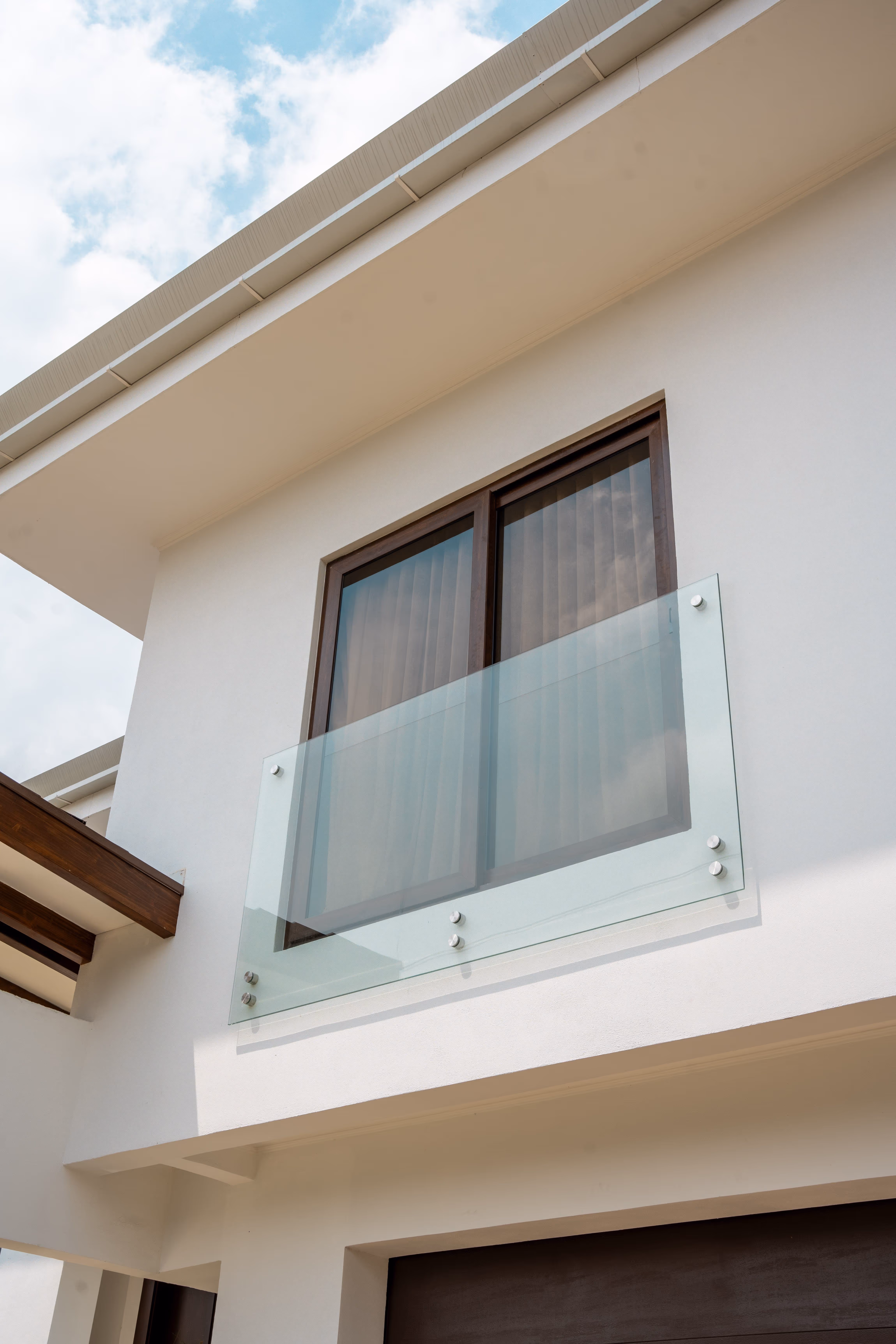 Balcón con barandilla de vidrio y ventana con marco de pvc imitación madera en una fachada blanca.