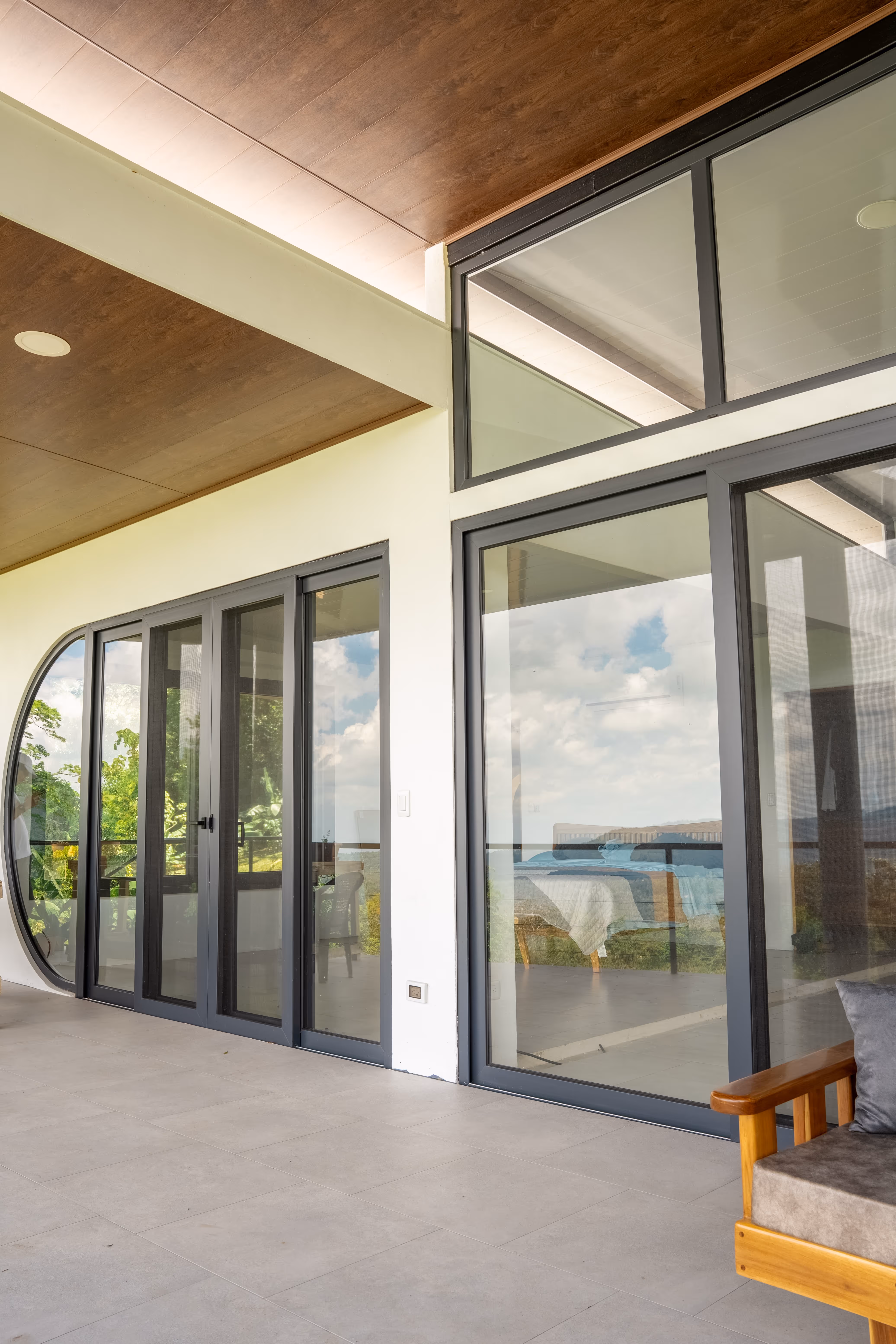 Terraza moderna con puertas corredizas de vidrio gris en pvc y sofá de madera con cojín gris.