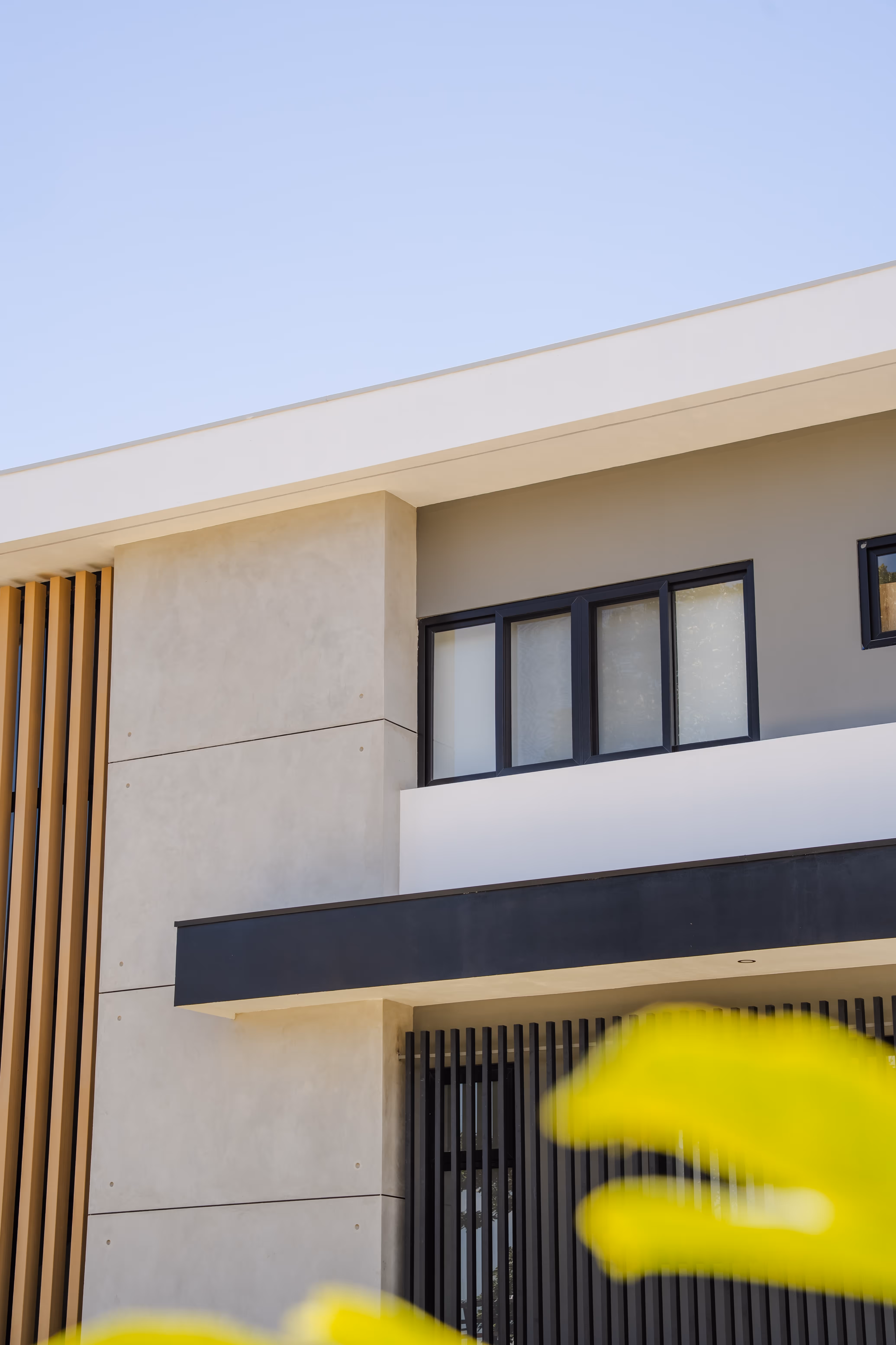 Fachada moderna de casa con ventanas negras corredizas de pvc, detalles verticales de madera y diseño minimalista.