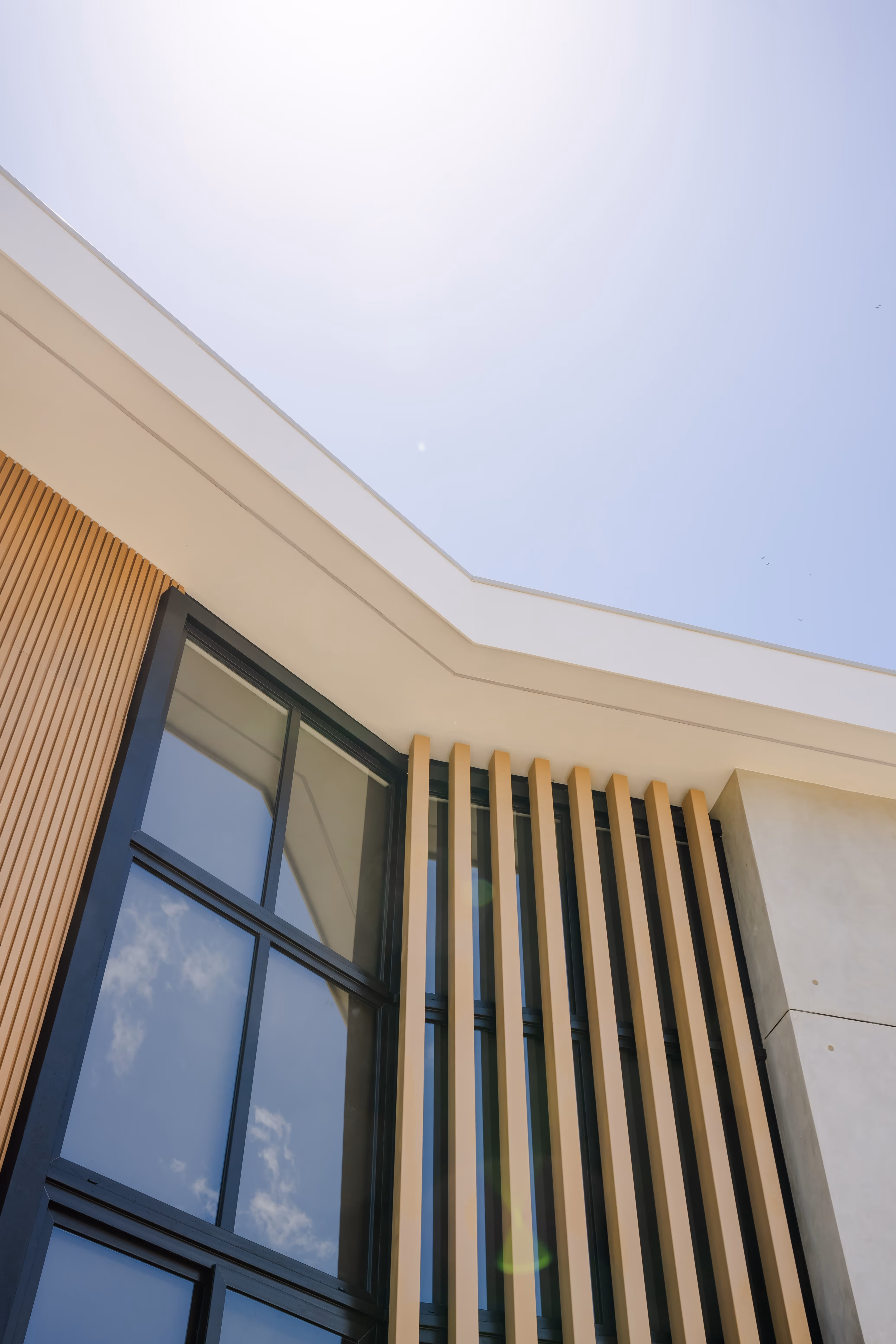 Detalle de la fachada moderna con ventanas grandes de pvc y paneles verticales de madera bajo un cielo claro.