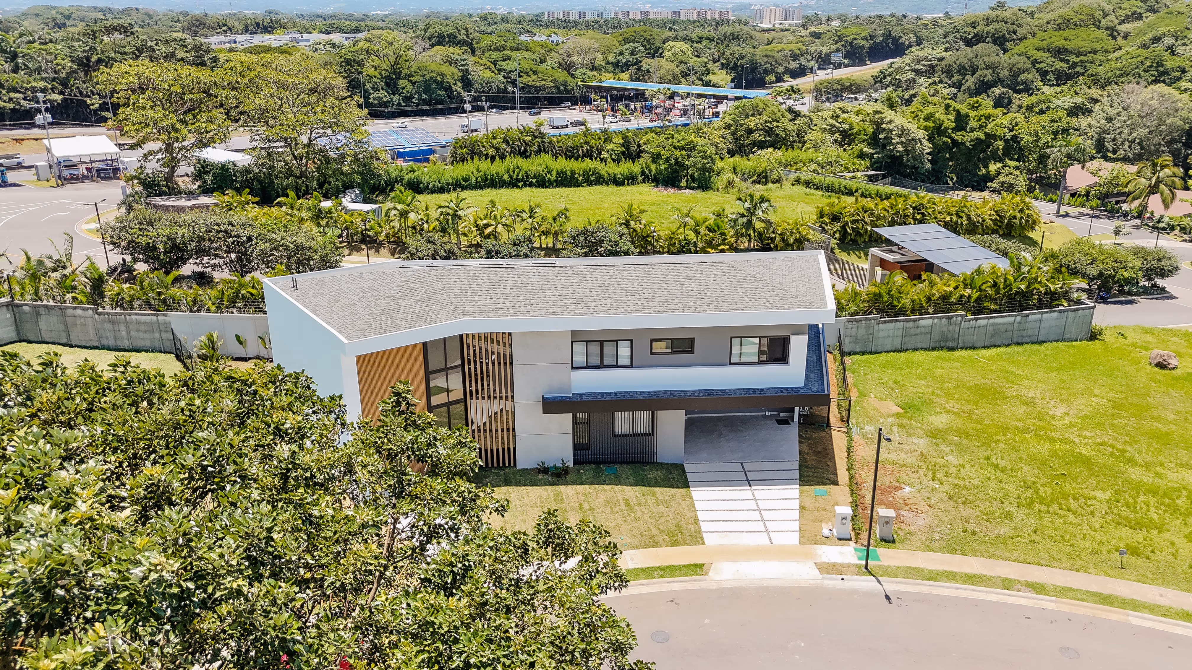 Casa moderna de dos pisos con techo gris, ventanas de pvc negro, ubicada en un barrio rodeado de árboles y áreas verdes.