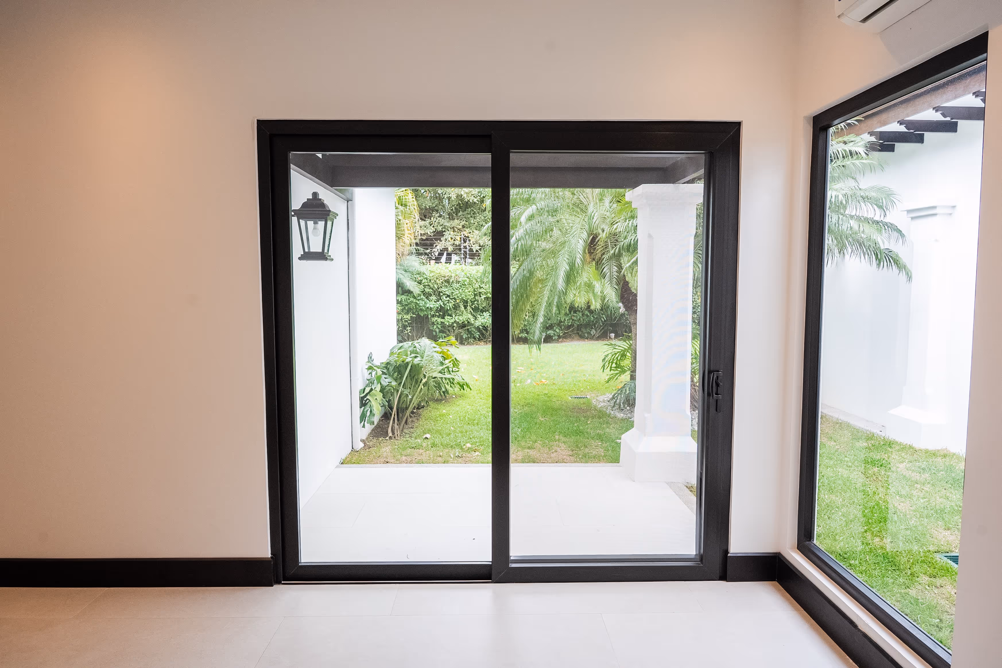Puerta corrediza de vidrio con marco negro de pvc que da a un jardín con césped y plantas, junto a una gran ventana lateral.
