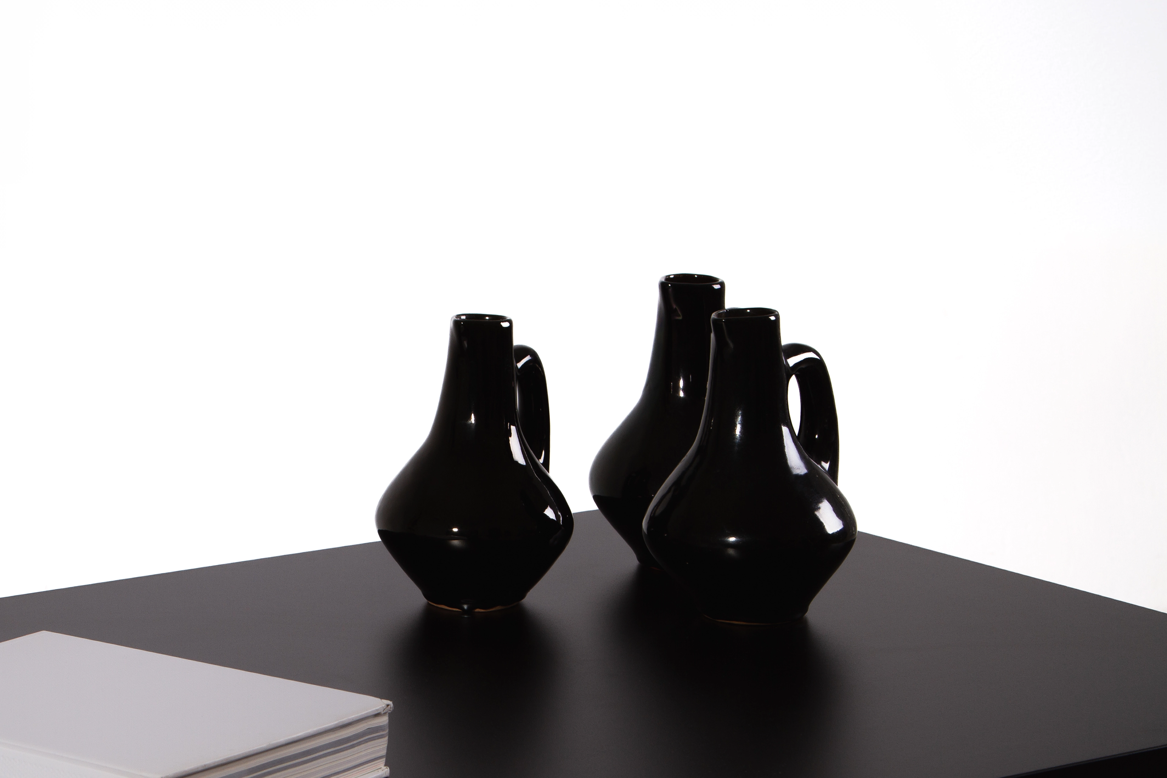 Cztery czarne ceramiczne dzbanki ustawione na ciemnym blacie