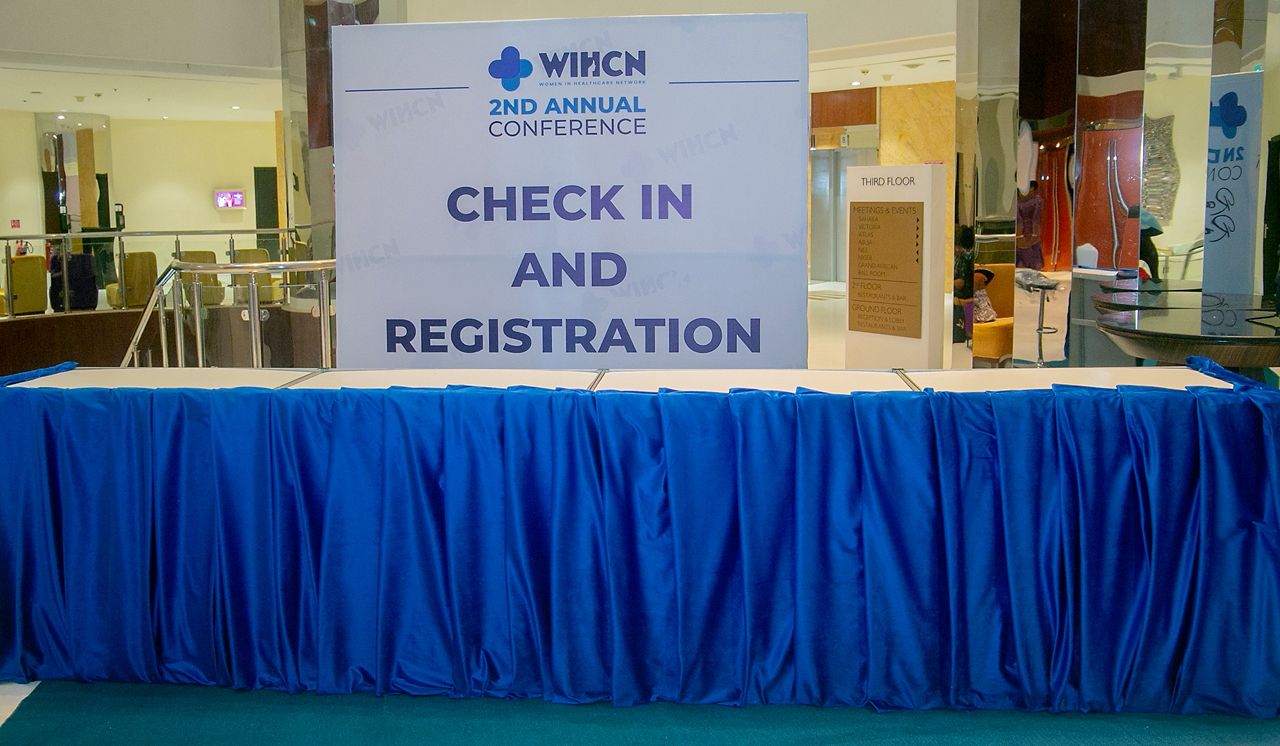 Event check-in table draped in blue cloth with a sign reading 'WIHCN 2nd Annual Conference Check In and Registration'.