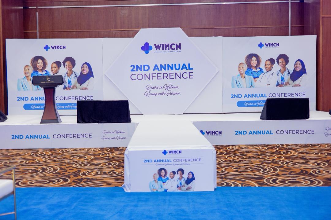 Conference stage setup with banners displaying '2nd Annual Conference' and diverse group of smiling women healthcare professionals.