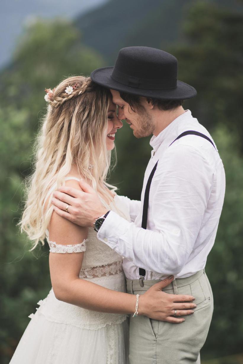 Nahaufnahme eines Paares im Freien mit lächelnder Braut und Bräutigam mit Hut und Hosenträgern.