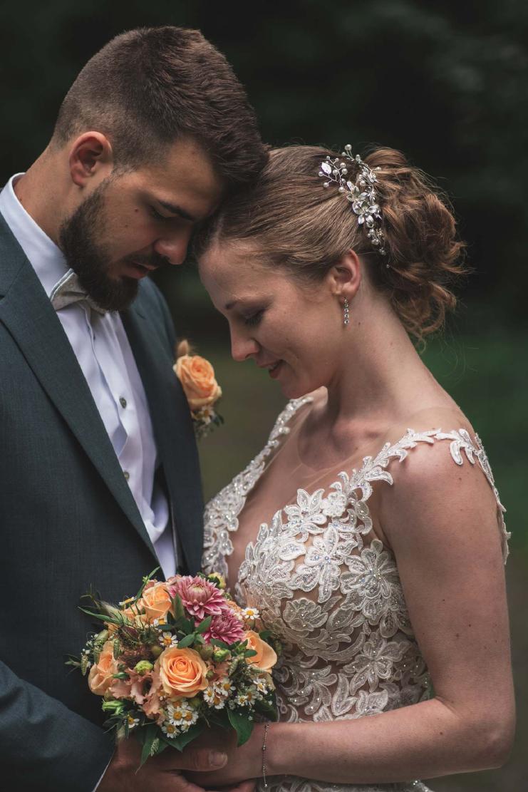 Emotionales und intimes Portrait des Brautpaares, die Stirnen aneinander gelehnt, die Braut trägt einen aufwendigen Haarschmuck in ihrer Steckfrisur und ein Spitzenbrautkleid. Keywords: Intime Hochzeitsfotos, Hochzeitsdetails, emotionale Hochzeitsreportage.