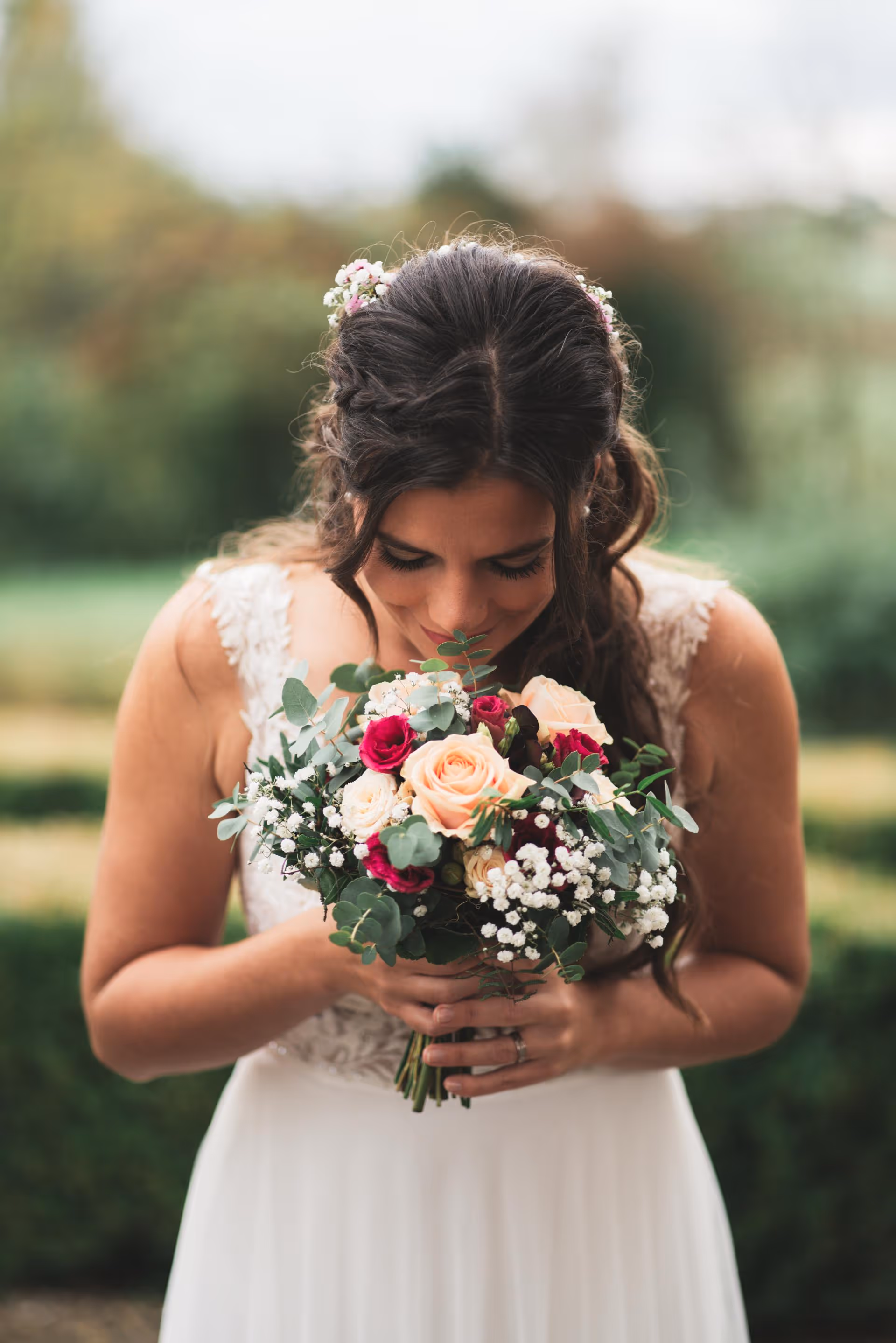 Nahaufnahme der Braut, die an ihrem Brautstrauß riecht. Detailaufnahme von Rosen in Pfirsich- und Burgunderrot mit Eukalyptus. Keywords: Brautstrauß-Ideen, Hochzeitsdetails, emotionale Brautbilder.