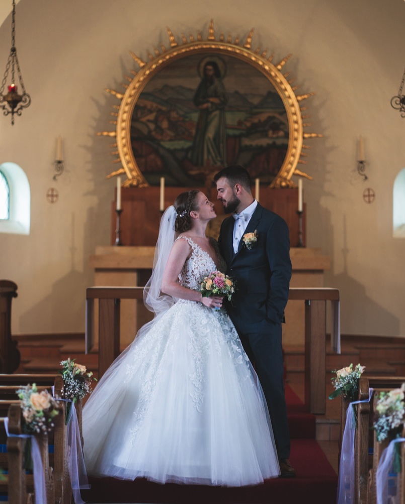 Emotionales Portrait eines Brautpaares in der Kirche nach der Trauung. Die Braut trägt ein voluminöses Brautkleid im Prinzessinnen-Stil mit Schleier.