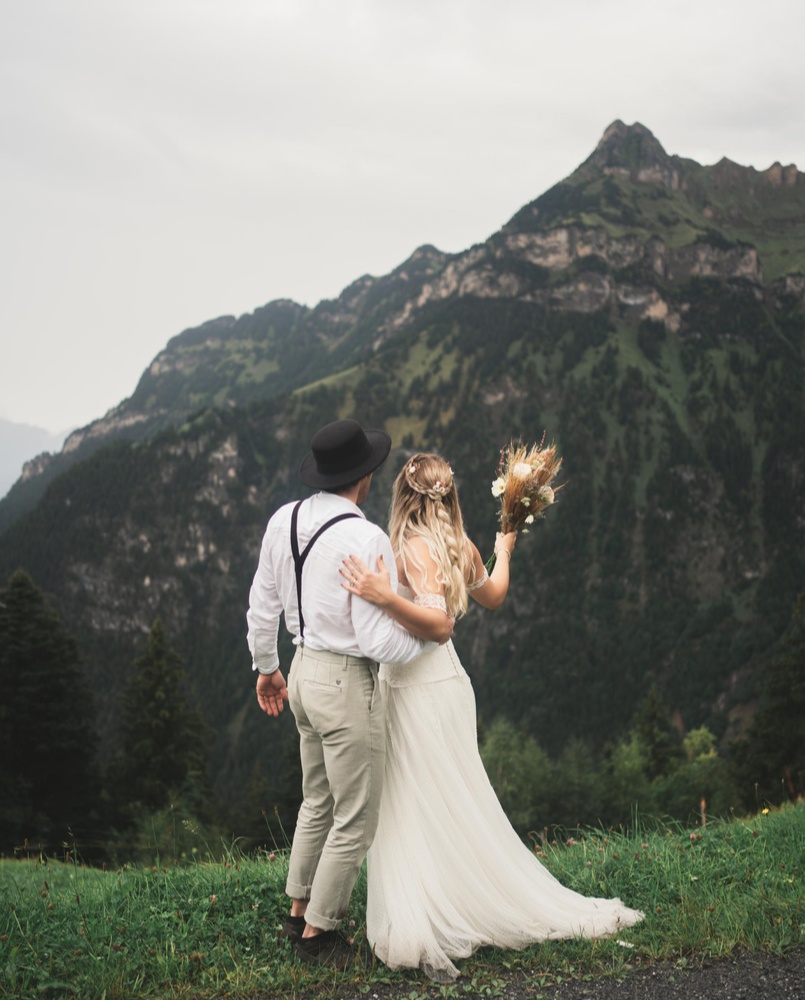 Brautpaar blickt gemeinsam auf die Berge während ihres Hochzeitsshootings in der Natur.