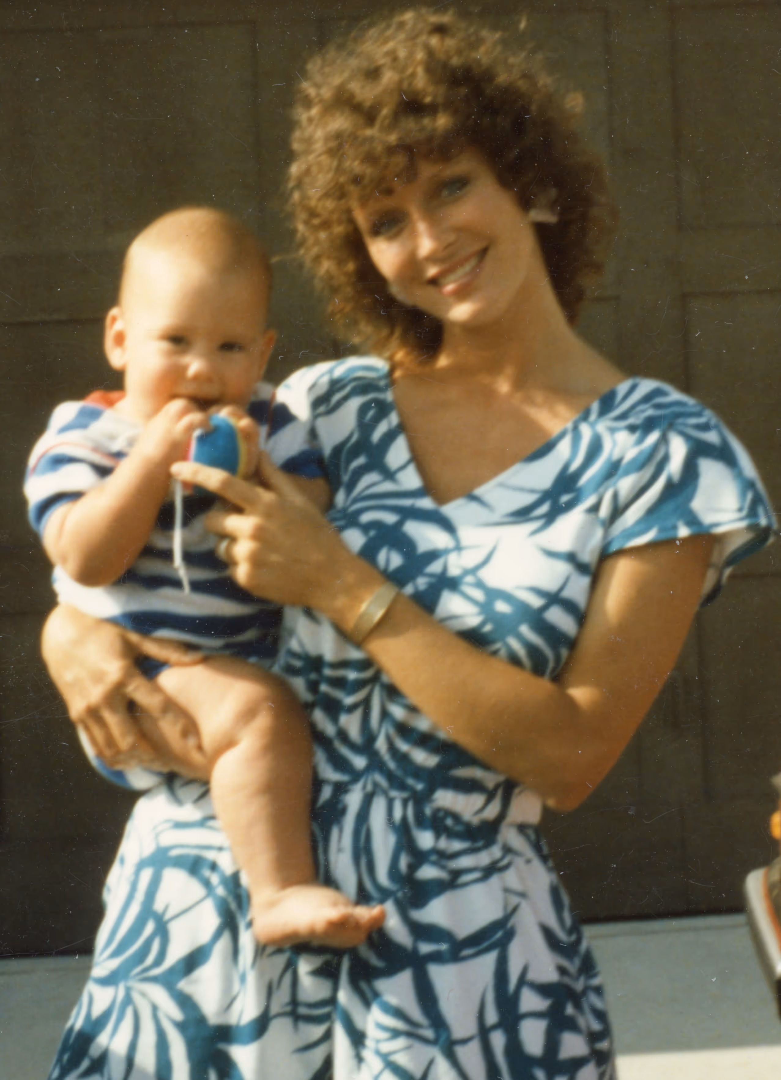 Susan Markowitz smiling in a dress holding baby Nicholas on her hip.
