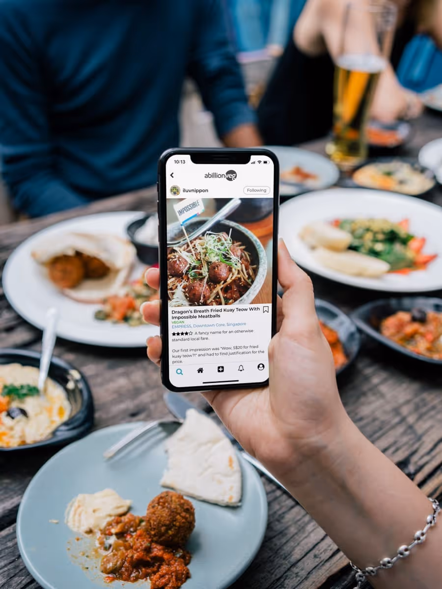 Persoon houdt telefoon vast met veganistisch eten op de achtergrond van een restaurantmaaltijd.