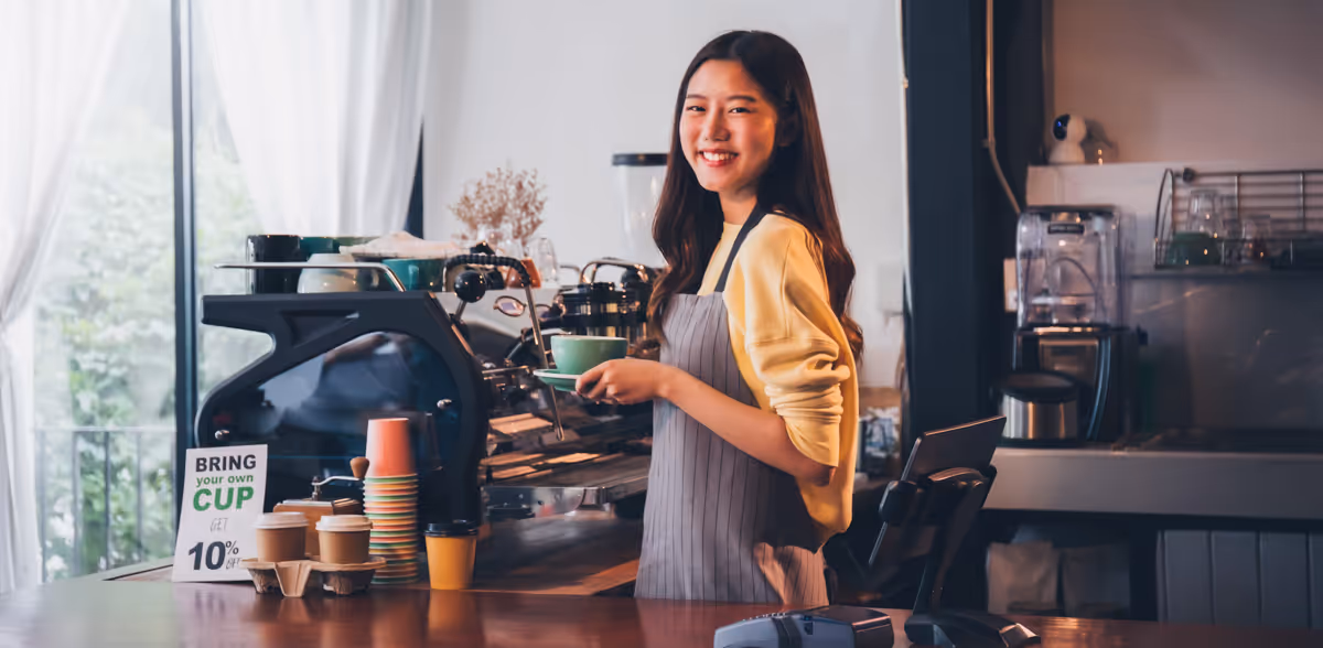 Vriendelijke barista achter de toonbank in het café met milieuvriendelijke bekers en duurzame koffieservice.