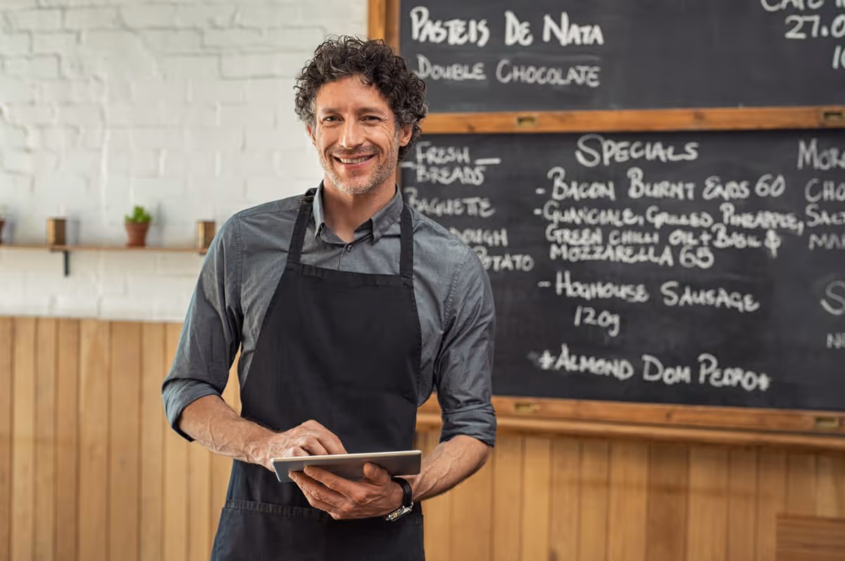 Lachende chef-kok in een zwart schort in een gezellig café met een krijtbordmenu.