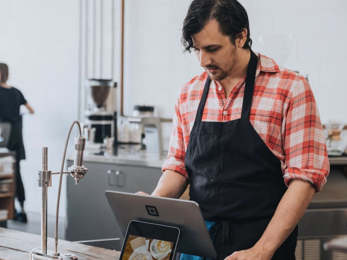 Een man met een schort werkt op afstand aan de balie van een koffiebar en bestelt online.