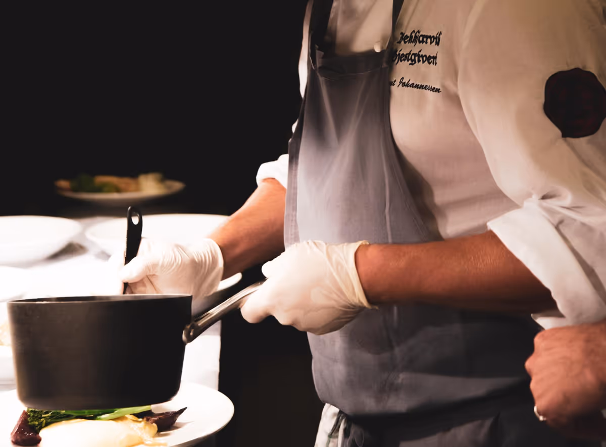 De chef-kok giet vakkundig een pittige saus over sappig vlees en verse geroosterde groenten.