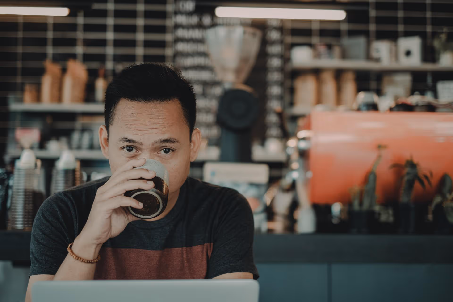 Man geniet van koffie terwijl hij op afstand op een laptop werkt in een modern koffiehuis.
