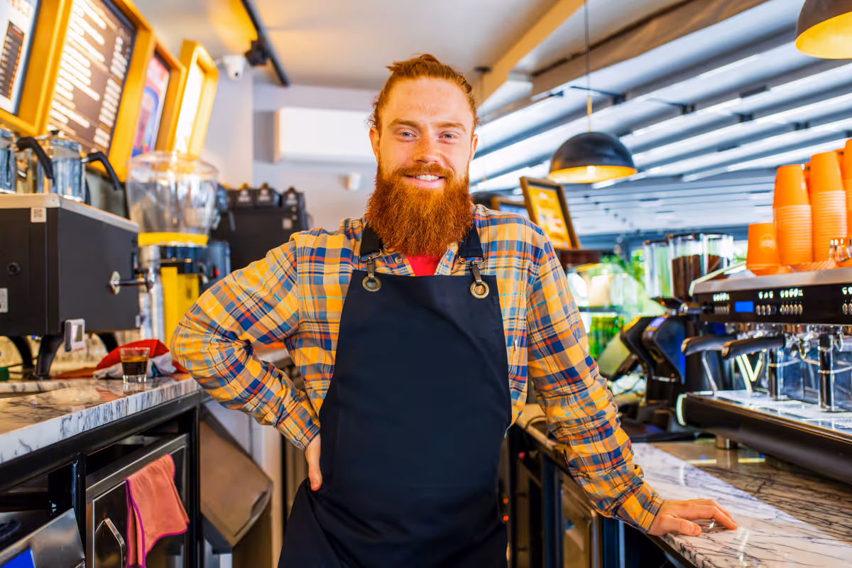 Vriendelijke barista met een verzorgde baard die vakkundig koffie zet in een gezellig koffiehuisje.