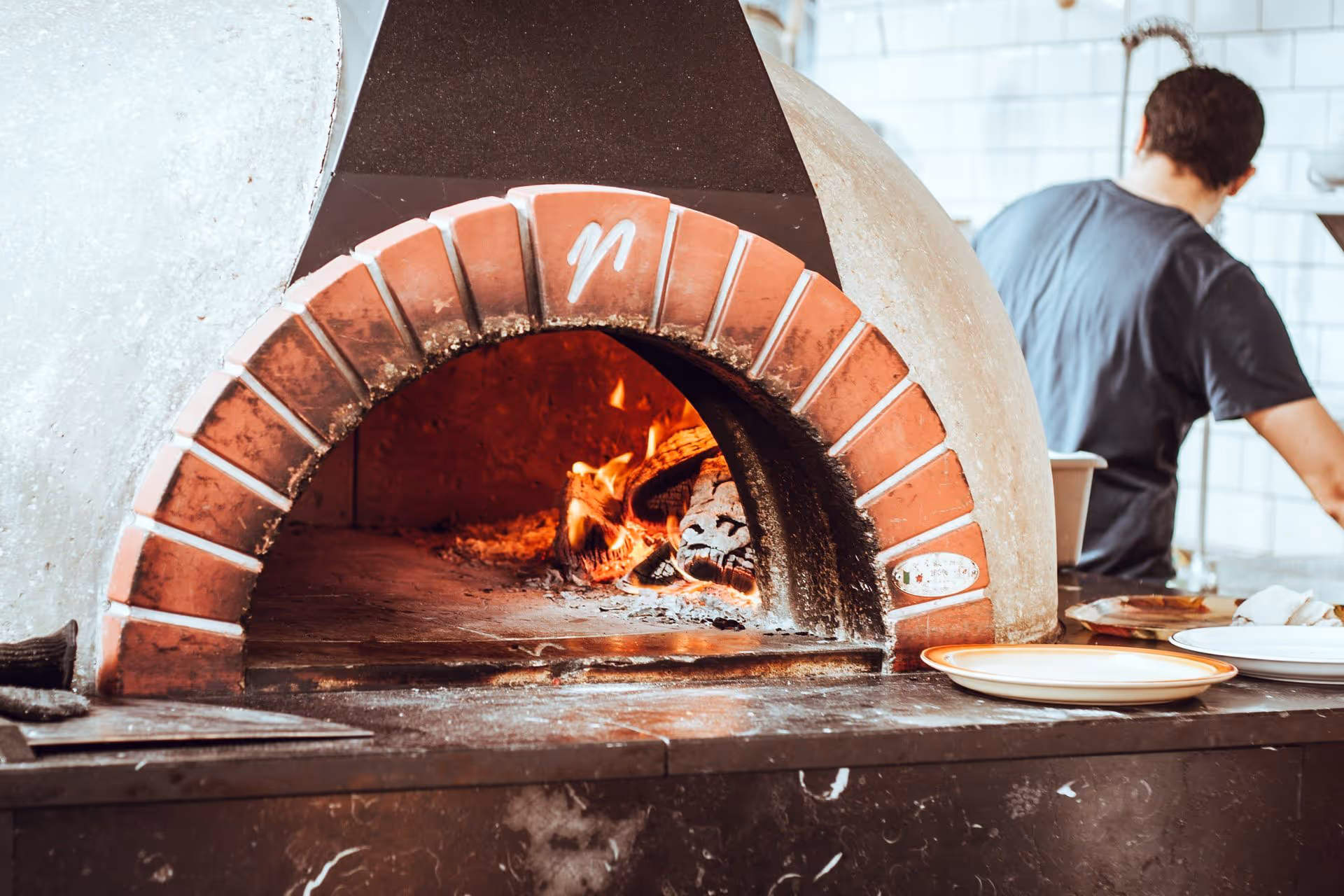De chef-kok bakt vakkundig pizza's in een houtgestookte steenoven, terwijl er vlakbij levendige vlammen branden.