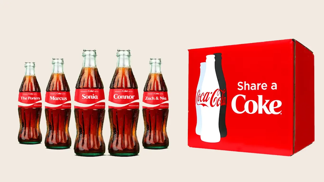 Five Coca-Cola glass bottles with personalised Share a Coke name labels lined up beside a red Share a Coke branded box.