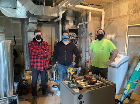 Three workers in masks standing in mechanical room with tools and equipment