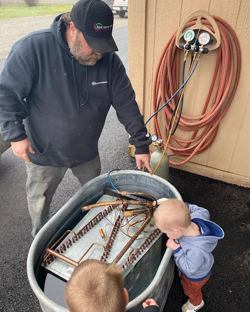 Worker with children examining equipment in metal tub near coiled hose