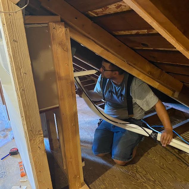 Person installing insulation or cable in wooden attic crawl space