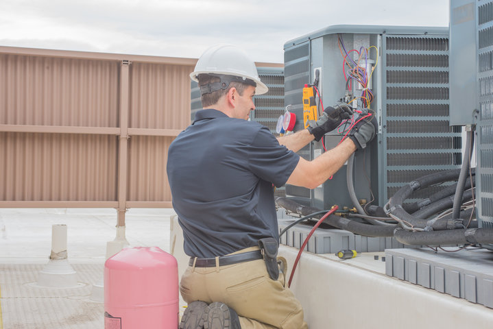 Technician in hard hat checking electrical connections on outdoor HVAC unit