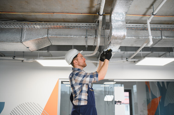 Worker in hard hat inspects industrial ceiling ventilation system