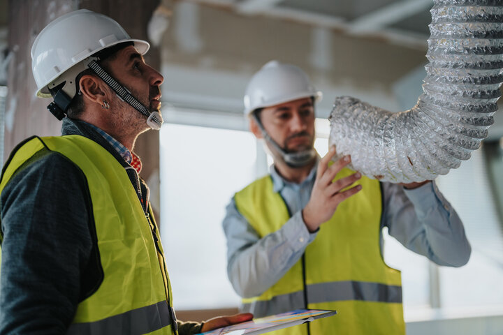 Construction workers in safety vests inspect large ventilation ductwork