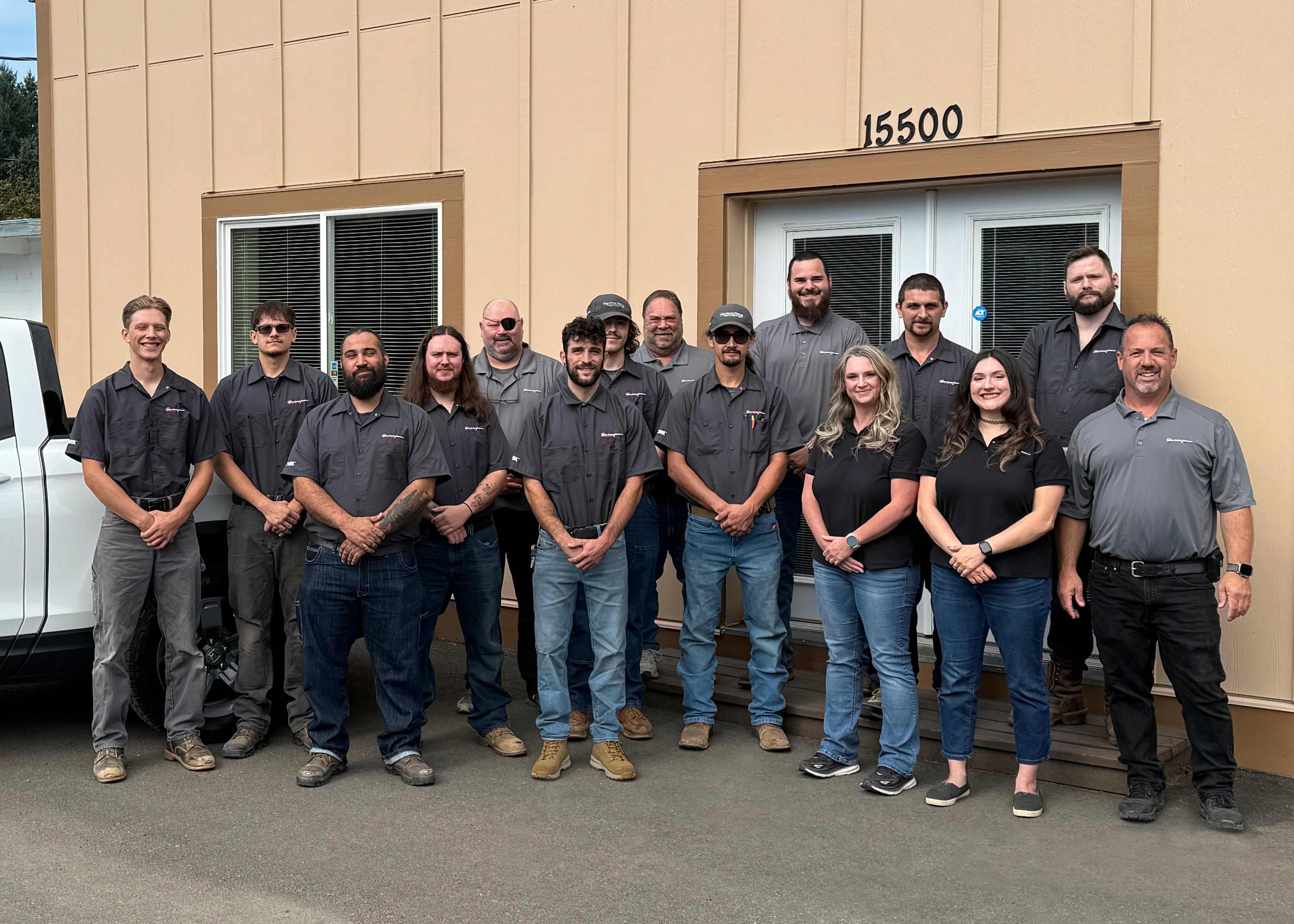 Team of technicians in matching gray shirts posing outside company building