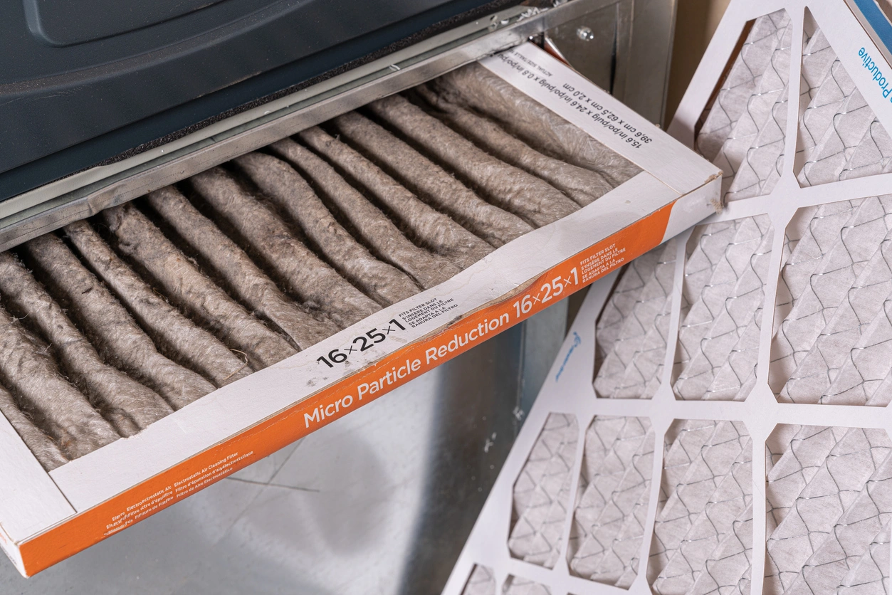 A dirty air filter is being removed from a furnace, showing accumulated dust and debris. 